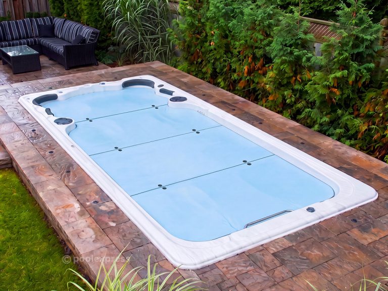 Pool Express - A rectangular swim spa, secured with an Insulating Spa Cover, is set in a patio surrounded by greenery, with a black outdoor sofa set nearby.