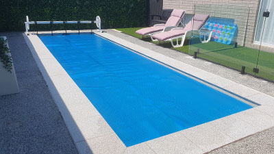 Pool Express - A rectangular backyard pool with a blue pool cover, two pink lounge chairs, a fence, and a colorful inflatable mat nearby.