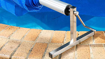 Pool Express - A metal pool cover roller with a hand crank is positioned at the edge of a brick-surrounded swimming pool.